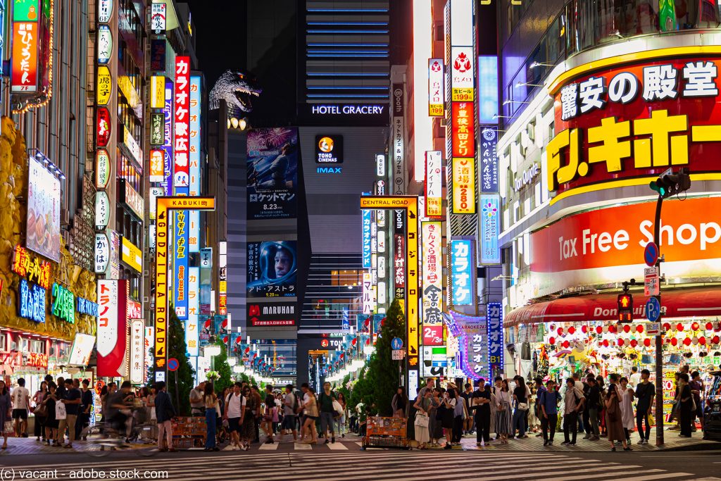pedestrians crossing a street in Shinjuku at night with the buildings all lit up in neon lights