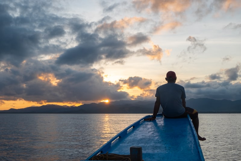 a man sitting on the end of boat at sunset