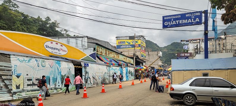 a street lined with shops, filled with people walking, and a sign saying Welcome to Guatemala