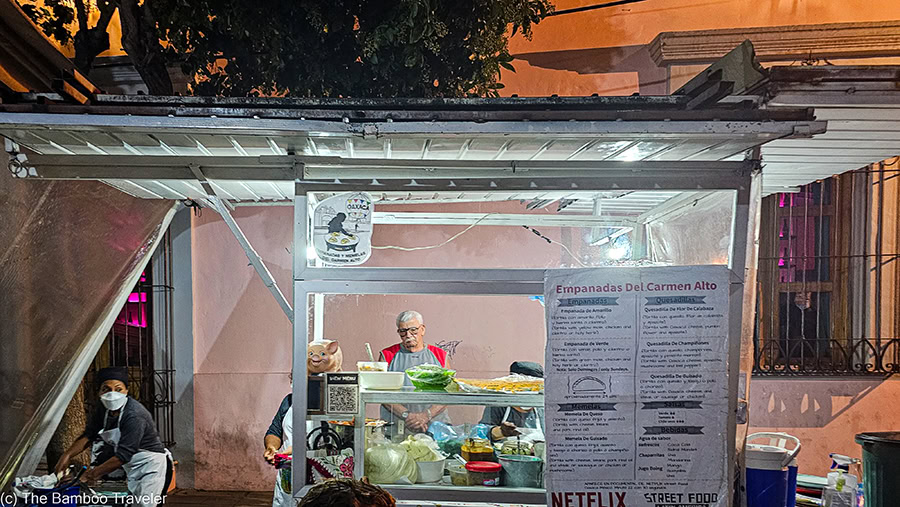 A person standing behind a food cart at night