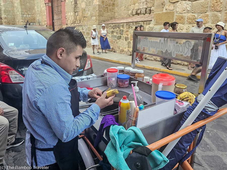 a man cutting a banana at a street food cart in Oaxaca