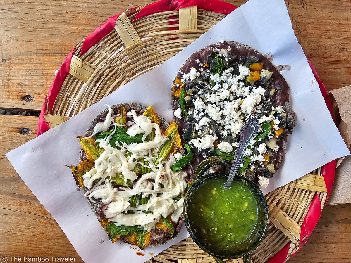 2 Oaxacan memelas and a bowl of green salsa on a plate