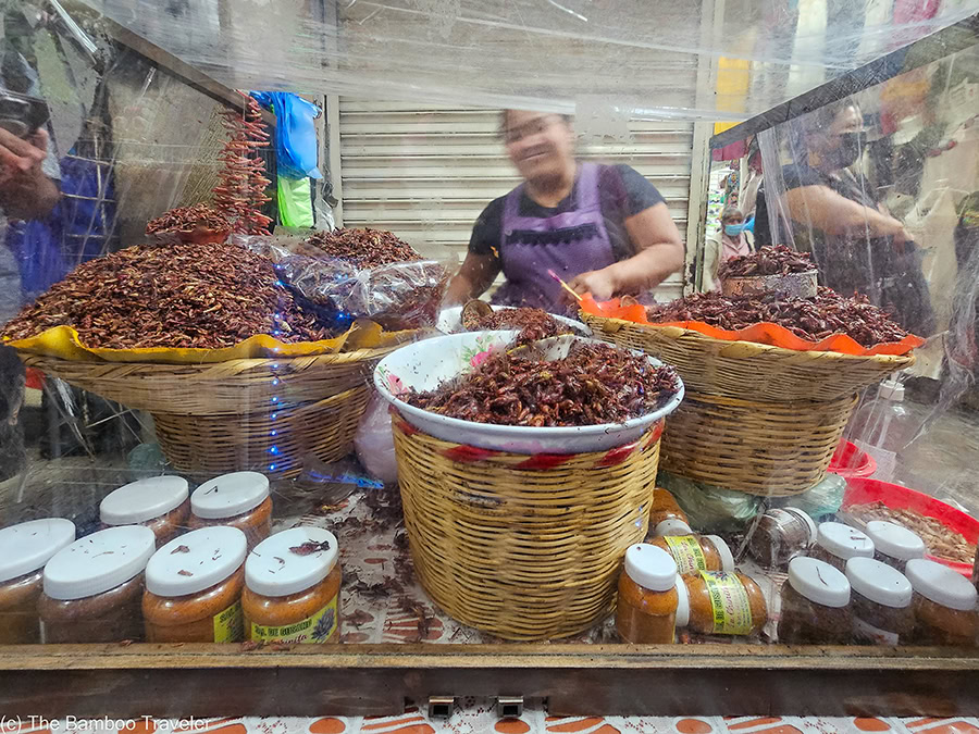 a woman standing behind a stand selling grasshoppers