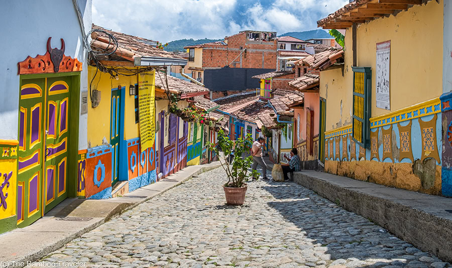 a cobblestone street going downhill and lined with colorful buildings with red tile roofs