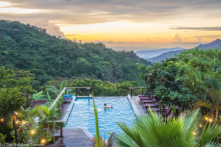 a person swimming in an infinity pool overlooking lush mountains at sunset