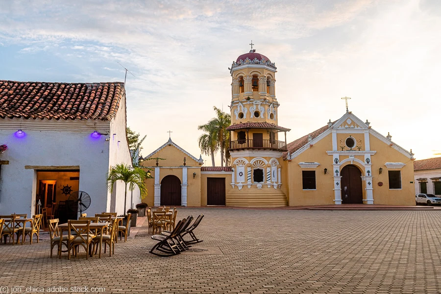 a plaza with a yellow church and a restaurant with tables outside in Mompox, Colombia