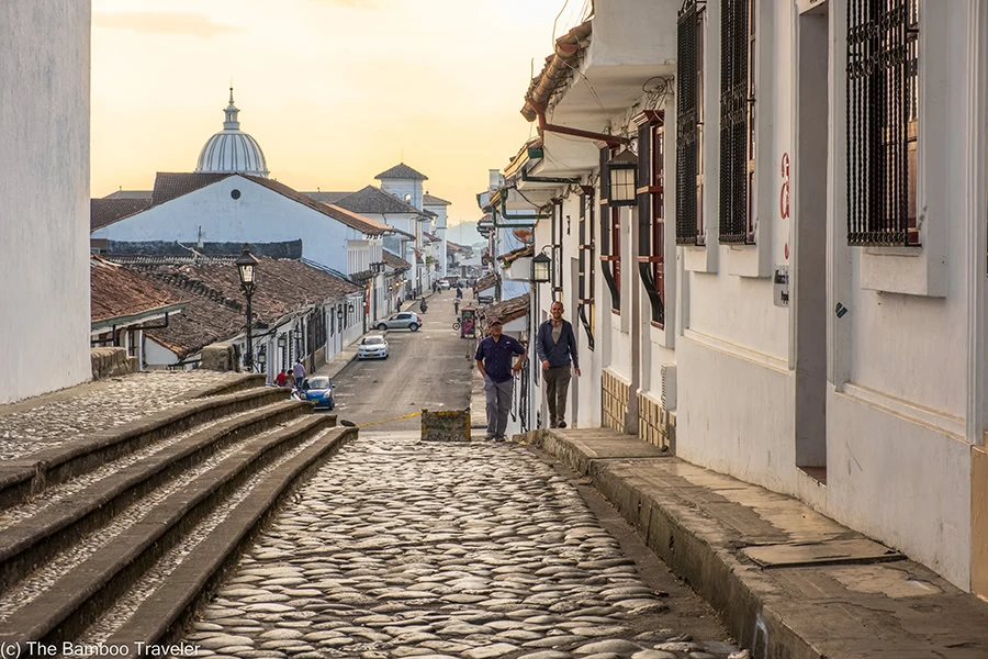 a cobbelstone street lined with white washed buildings at with the sun setting in the background