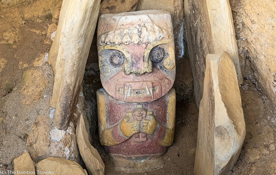 an ancient short stone statue of a monster with fangs and big round eyes.