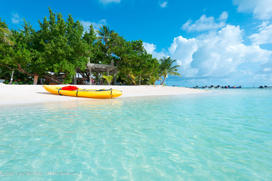 a kayak on a white sandy beach next to crystal clear water