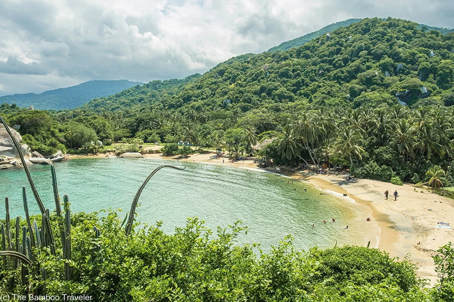 a bay with a white sandy beach and a hill covered in trees behind the bay