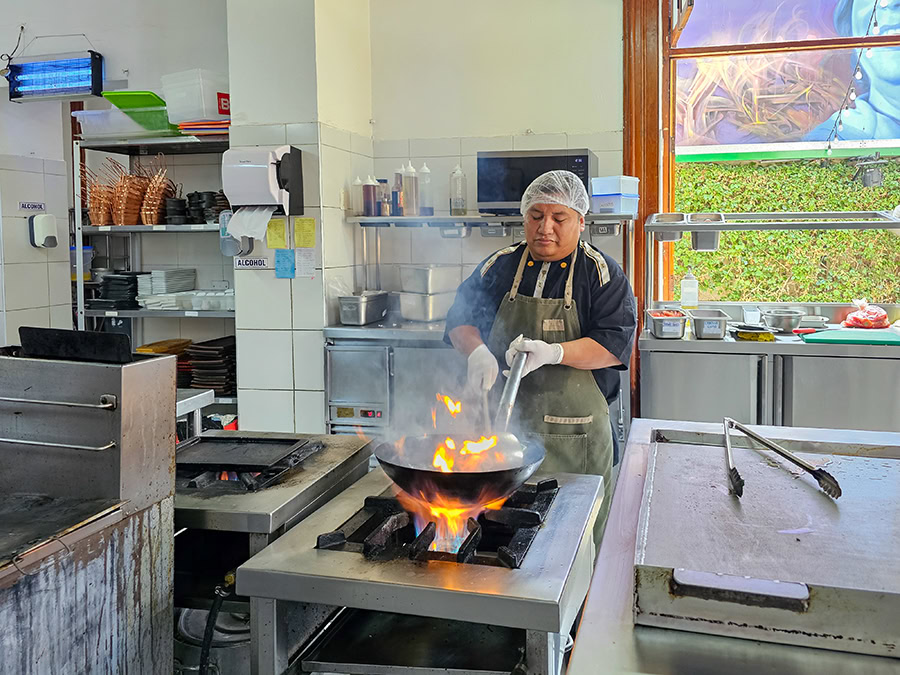 Flames are jumping out of a wok as a male chef is stir frying lomo saltado in a wok on a restaurant kitchen