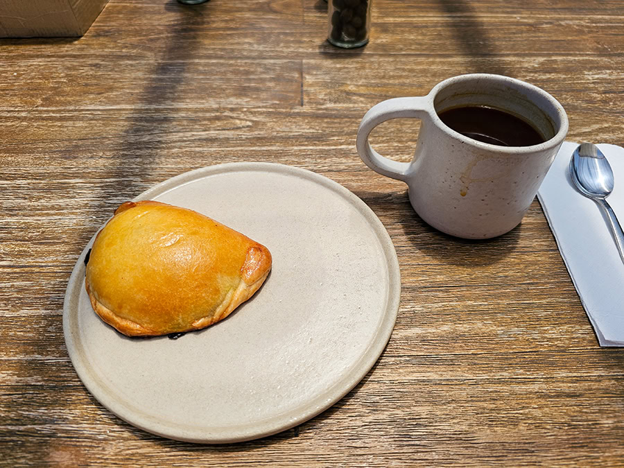 an empanada on a plate and a cup of coffee