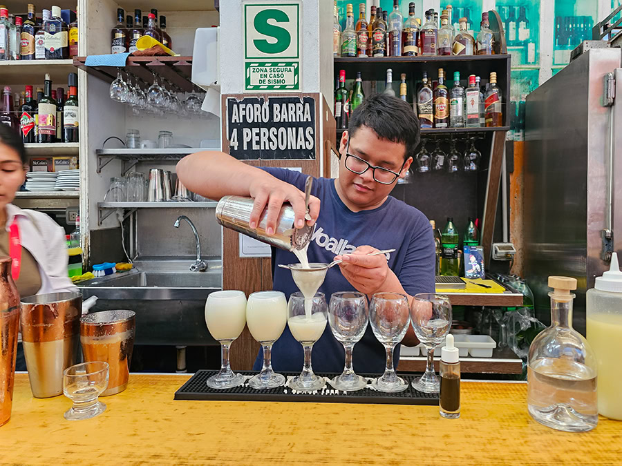 a bartender pouring pisco sour from a shaker through a strainer and into a glass