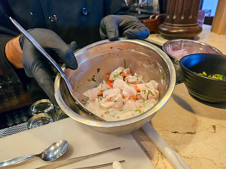Two gloved hands holding a bowl of raw fish in tiger's milk