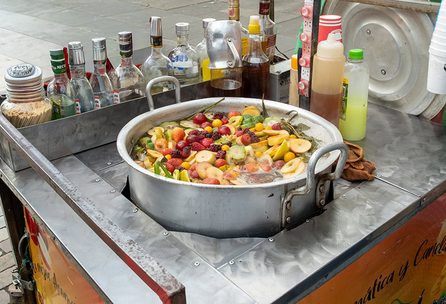 Traditional Colombian Canelazo being prepared on the streets of Bogotá. A vibrant, fruit-filled pot of the spiked cinnamon drink during a local walking tour.