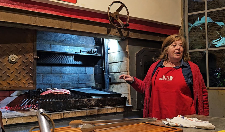 Betty is standing next to the parrilla and pointing at it.