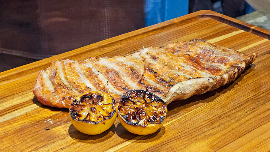 A perfectly grilled Argentine matambre rests on a wooden carving board alongside two charred lemon halves. This traditional dish was prepared over an open fire during Betty and Marcelo's Asado Food Tour in Buenos Aires, Argentina.