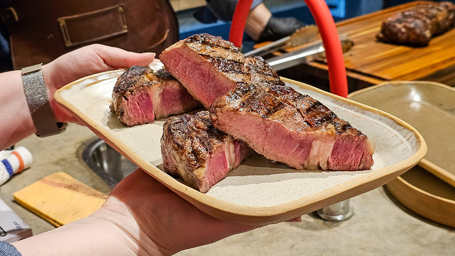 A close-up shot of thick slices of medium-rare Argentine ribeye (ojo de bife) held on a ceramic plate during Betty and Marcelo's Asado Food Tour in Buenos Aires. The steak features deep char marks from the parrilla (grill) and a perfectly pink center, highlighting the high-quality Argentine beef served in this private culinary experience.