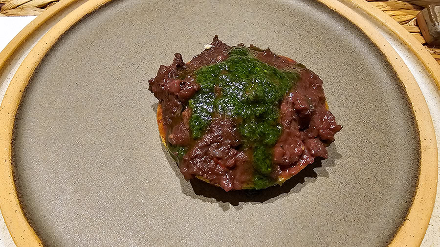 A close-up shot of a traditional Argentine morcilla (blood sausage) spread served on a small piece of toasted bread, topped with fresh green chimichurri sauce. 