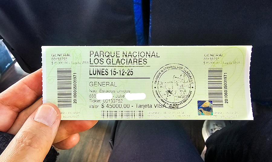 a light green entry ticket for Parque Nacional Los Glaciares in Argentina, held between a person's thumb and index finger. The ticket features bold black text at the top: "PARQUE NACIONAL LOS GLACIARES" and "LUNES 15-12-25". Below, the ticket lists "GENERAL", "Nac. Estados Unidos", "Julie", "Ticket: 00133752", and "Valor: $ 45000.00 - Tarjeta VISA". There are two vertical barcodes and a circular official seal of the Administración de Parques Nacionales on the ticket.