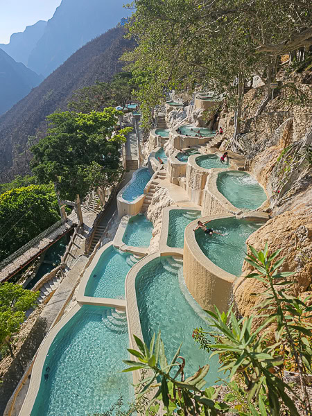 A vertical high-angle view of the terraced turquoise thermal pools cascading down the rugged canyon cliffside at Grutas Tolantongo